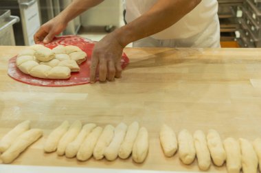 Becerikli fırıncı ahşap bir yüzey üzerinde hamur şekillendiriyor, yakınlarda düzgün düzenlenmiş ekmek ruloları var, mutfak sanatını gösteriyor..