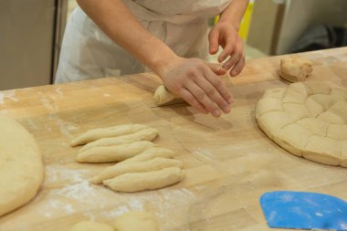 Baker is skillfully shaping dough on a wooden surface, surrounded by flour and baking tools, creating a warm kitchen atmosphere.