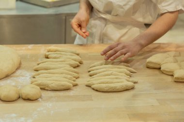 Individual is shaping dough on a wooden surface, surrounded by flour and freshly prepared bread, showcasing culinary skills.