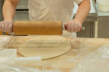 Baker skillfully rolls out dough on a wooden countertop, surrounded by flour and kitchen tools, showcasing culinary expertise.