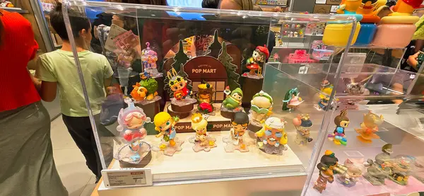 Berlin, Almanya. 27 Ağustos 2025. Market içi ziyaretçileri bakınıyor. Raflarda koleksiyon figürleri ve ürünler sergilenirken, cam anonslarda satılan Labubu serileri çeşitli tabelalar yer alıyor.