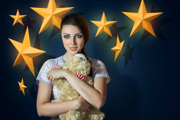 若いですブルネット女性身に着けていますPajama巨大テディベアでザベッドルームで装飾された星で背景 — ストック写真