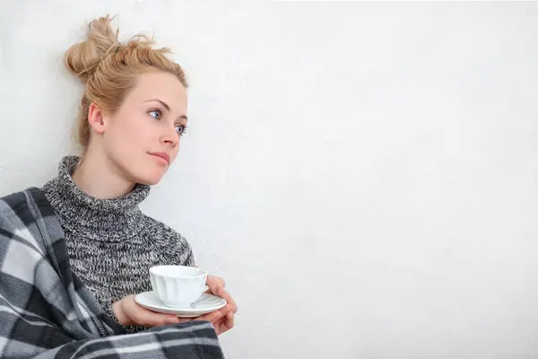 一个年轻的女人享受片刻的放松 坐在地板上 靠着一面白色的墙 喝一杯咖啡或茶 生活方式或与饮料有关的概念的平静和舒适的气氛 图库照片