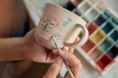 Close up shot of a woman potter painting a cup in her crafts workshop