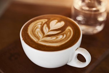 Tahta masadaki sıcak latte sanat kahvesine odaklan, beyaz köpüğe odaklan.