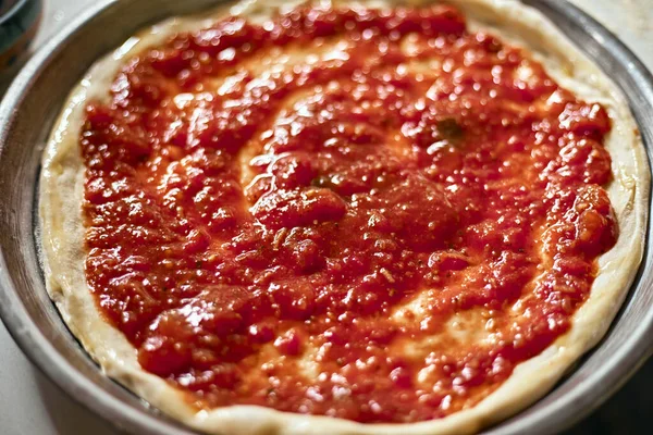 Spreading tomato sauce on pizza pan, selective focus