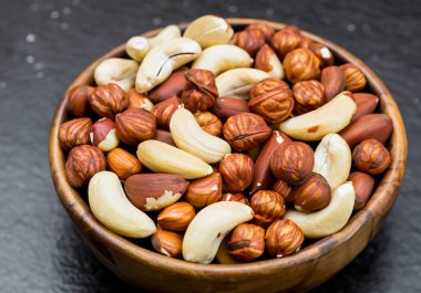 Koyu taş masada, tahta kasede fındıklar.