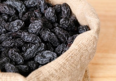 Çuval bezinde siyah kuru üzümler, ahşap masanın üzerinde.