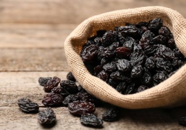 Çuval bezinde siyah kuru üzümler, ahşap masanın üzerinde.