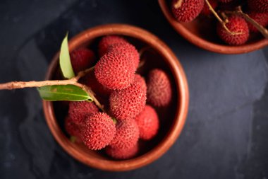 Koyu arkaplanda yaprakları olan taze kırmızı liçi meyveleri..