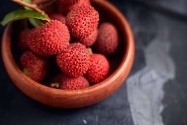 Koyu arkaplanda yaprakları olan taze kırmızı liçi meyveleri..