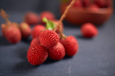 Koyu arkaplanda yaprakları olan taze kırmızı liçi meyveleri..