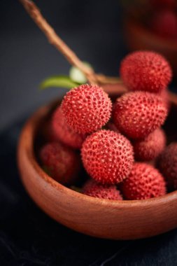 Koyu arkaplanda yaprakları olan taze kırmızı liçi meyveleri..