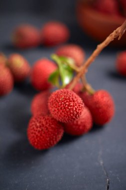 Koyu arkaplanda yaprakları olan taze kırmızı liçi meyveleri..