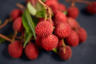 Koyu arkaplanda yaprakları olan taze kırmızı liçi meyveleri..