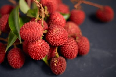 Koyu arkaplanda yaprakları olan taze kırmızı liçi meyveleri..