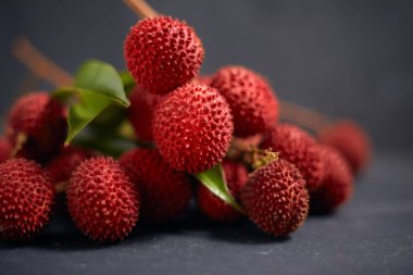 Koyu arkaplanda yaprakları olan taze kırmızı liçi meyveleri..