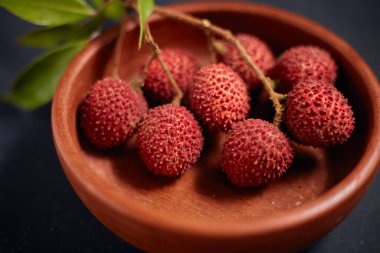 Koyu arkaplanda yaprakları olan taze kırmızı liçi meyveleri..