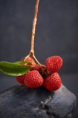 Koyu arkaplanda yaprakları olan taze kırmızı liçi meyveleri..