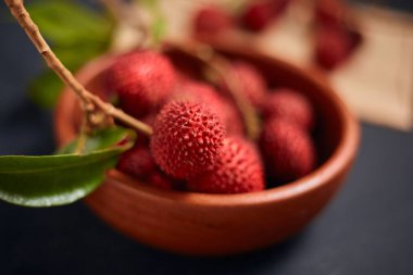 Koyu arkaplanda yaprakları olan taze kırmızı liçi meyveleri..