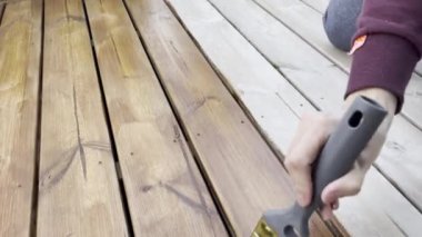 Bir adam ahşap güverteye leke sürer. Korunmak için güverteyi boyuyorum. Teras koruması.