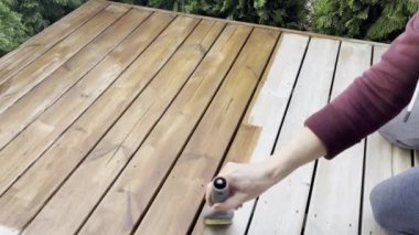 Bir adam ahşap güverteye leke sürer. Korunmak için güverteyi boyuyorum. Teras koruması.