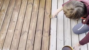 Bir adam ahşap güverteye leke sürer. Korunmak için güverteyi boyuyorum. Teras koruması.