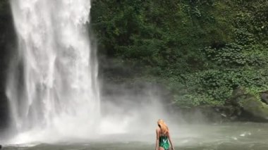 Canlı bir orman ortamında çarpıcı bir şelalenin yanında huzurlu bir an. Şelaledeki kadın. Bali. Ubud. 
