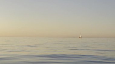 Huzurlu, yansıtıcı sularda bir yelkenlinin olduğu huzurlu bir günbatımı sahnesi..