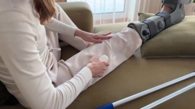 Oturma odasındaki kanepede oturan bir kadın bacağındaki kan dolaşımını iyileştirmek için perküsyon masaj aleti kullanıyor..