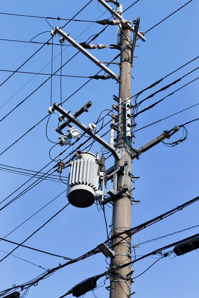 Electric wires on a pole with a transformer. Energy and technology, electric pole with power line cables, transformers and telephone lines on bright blue sky background. High quality photo.