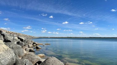 Mavi gökyüzü ve beyaz bulutlarla gölün kayalık kıyısı