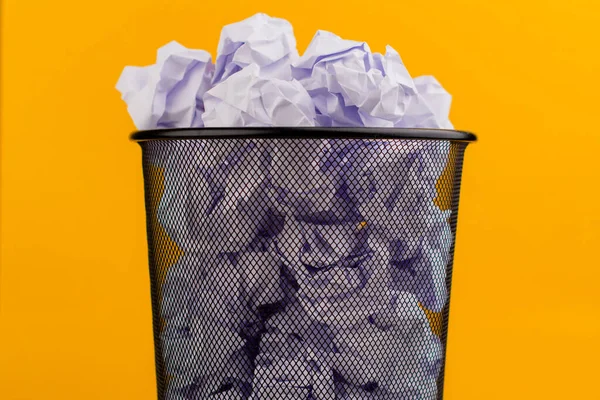 White scraps of paper in the trash can on a yellow background, waste paper waste concept