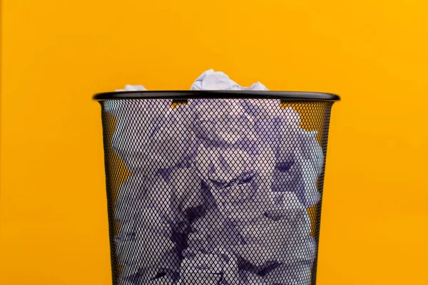 White scraps of paper in the trash can on a yellow background, waste paper waste concept