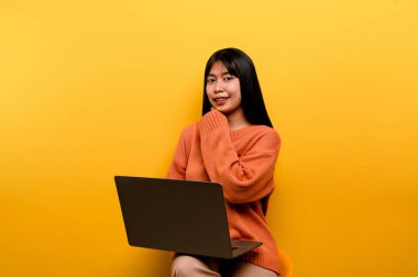 Asyalı bir kadın ve dizüstü bilgisayar ve evde çalışmaktan mutlu olan güzel bir Asyalı kadının fotoğrafını çekmekten mutlular. ev konseptinde dizüstü bilgisayar sarı stüdyo çalışması kullanarak