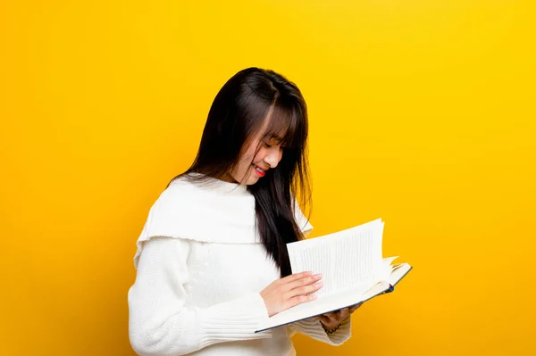 Read a book, study with the protagonist, seek knowledge, food for thought, girl reading a book and smiling. in the photo studio yellow backdrop