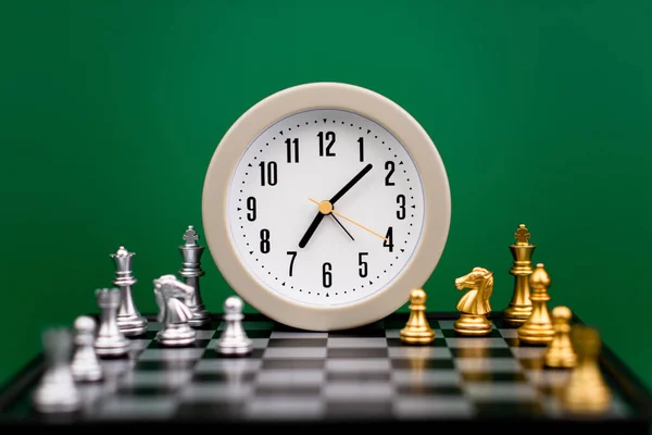 alarm clock on chess table time strategy plan work with time green backdrop Working with time. Be on time. Keep time. Value time concept.