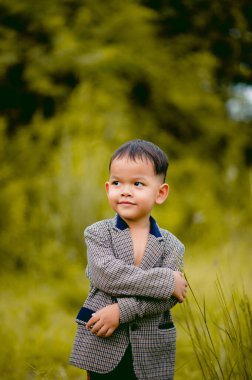 Şirin küçük bir çocuk. Arka bahçesinde takım elbiseli bir çocuk. Çimenli ve ilginç bir şey arıyor..