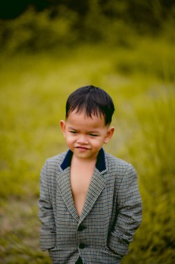 Şirin küçük bir çocuk. Arka bahçesinde takım elbiseli bir çocuk. Çimenli ve ilginç bir şey arıyor..