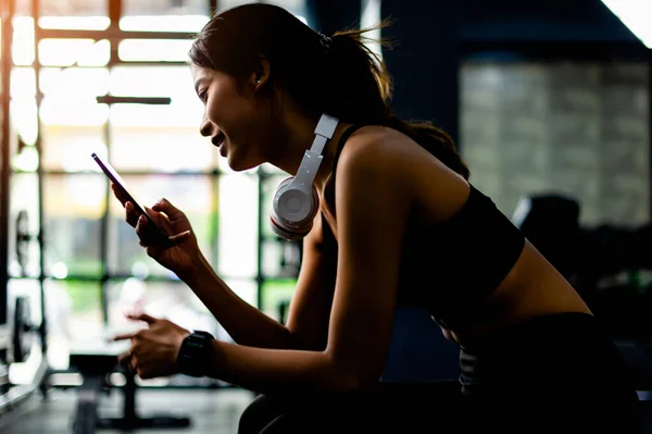 Asian woman in fitness clothes sitting on white phone and headphones relax during exercise create energy for exercise fitness inspiration