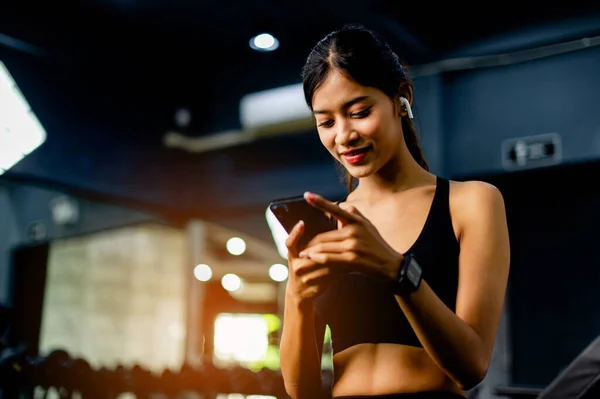 Asian woman in fitness clothes sitting on white phone and headphones relax during exercise create energy for exercise fitness inspiration