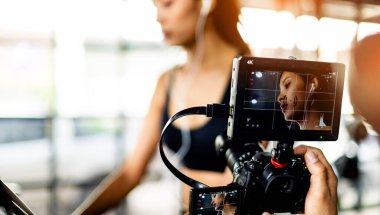 Koşu bandında koşan genç bir kadının perde arkasındaki film monitörü..