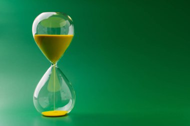 Kum saati sabit duruyor, zaman sınırı ve limitlerle çalışıyor, stüdyoda yeşil arka planda fotoğraf var.