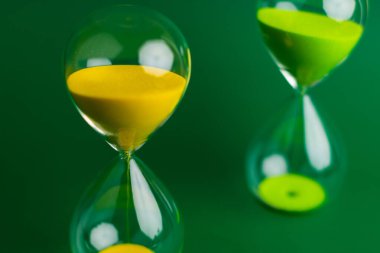 Sarı kum saati yeşil arka planda yakın plan fotoğrafı. Kaliteli iş ve zaman yönetimi kavramı.