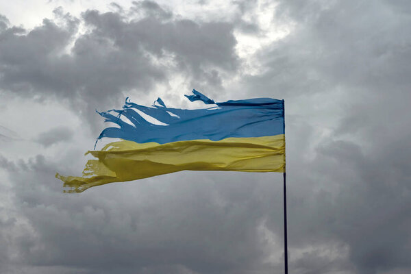 Tattered shabby Ukraine flag on gray cloudy sky as symbol of nation struggle and courage