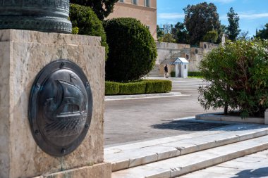 Bronze Shield representing an ancient greek ship at the entrance of the Unknown Soldier's Tomb memorial under the Greek parliament. Evzone in the background