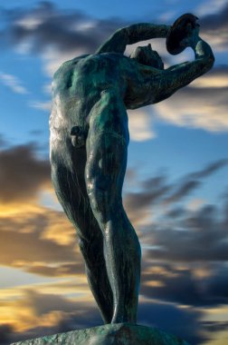 Atina, Yunanistan. Konstantinos Dimitriadis tarafından yapılan Discus Thrower heykeli. Panathenaic Stadyumu'nun karşısında. Yüksekliği 2 metreye ulaşır. Gün batımı zamanı, rengarenk bulutlu gökyüzü. Hareket bulanık gökyüzü