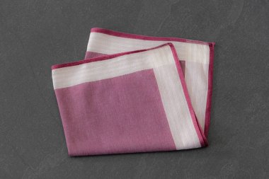 Çizgili desenli zarif katlanmış mendil, koyu taş bir yüzeyde sergileniyor. Erkeklerin moda aksesuarları, tarzı veya kumaş dokularıyla ilgili kavramlar için uygundur..