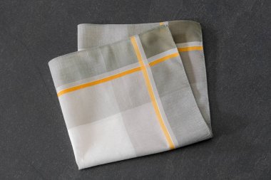 Çizgili desenli zarif katlanmış mendil, koyu taş bir yüzeyde sergileniyor. Erkeklerin moda aksesuarları, tarzı veya kumaş dokularıyla ilgili kavramlar için uygundur..