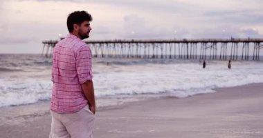 Okyanus kıyısındaki kumlu sahil şeridinde sörf yapan genç bir adam.